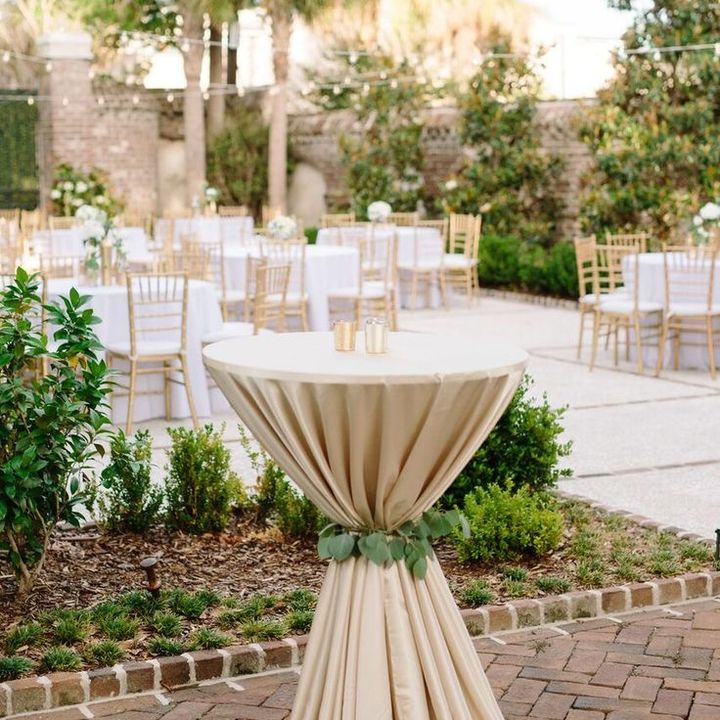 Mesa alta de cóctel con mantel en un jardín preparado para el evento